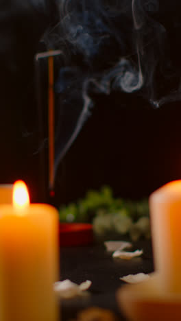 Vertical-Video-Still-Life-Of-Lit-Candles-With-Scattered-Petals-Incense-Stick-Against-Dark-Background-As-Part-Of-Relaxing-Spa-Day-Decor-1